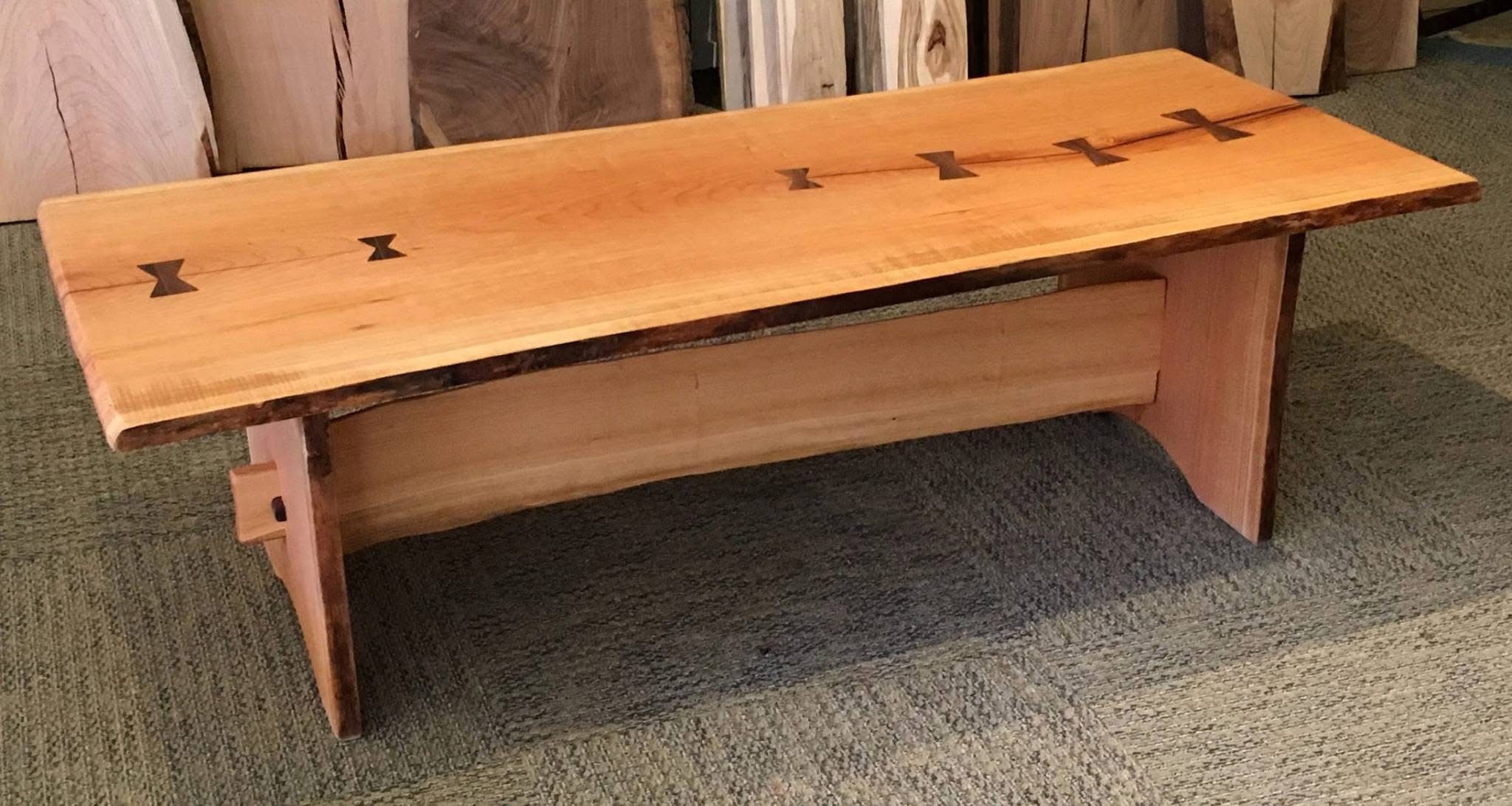A live edge bench made of cherry wood with two black walnut butterflies on the left side and four black walnut butterflies on the right side