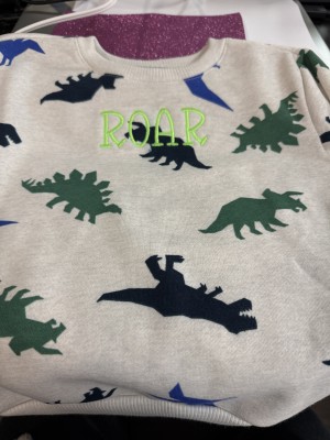 A toddler size dinosaur shirt with "ROAR" embroidered in bright green